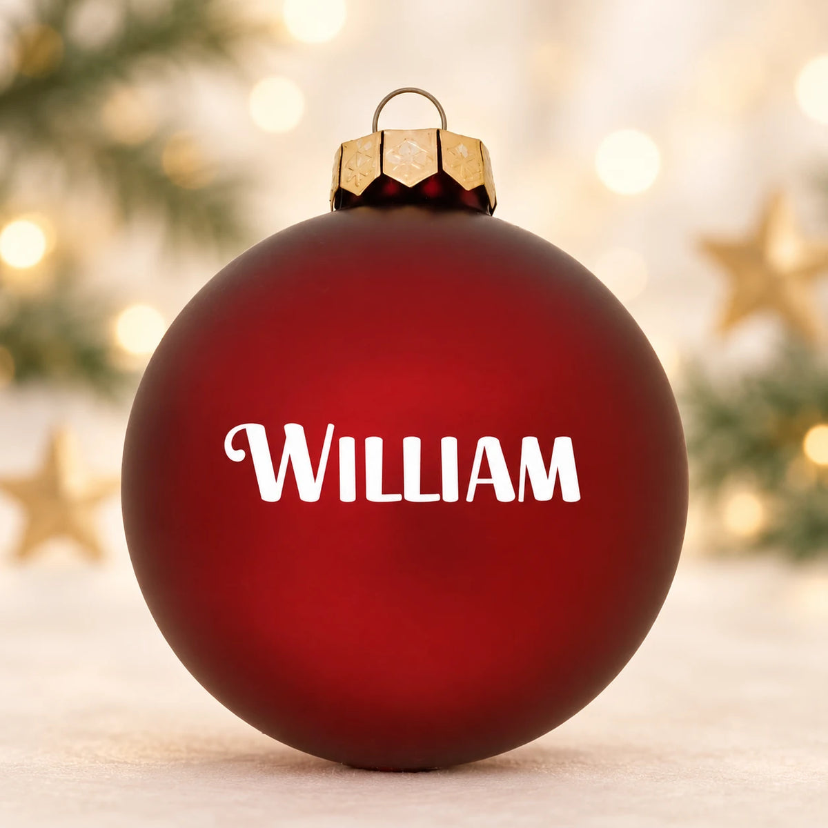 Mat rød julekugle med navnet William på diffus julebaggrund med gran og stjerner