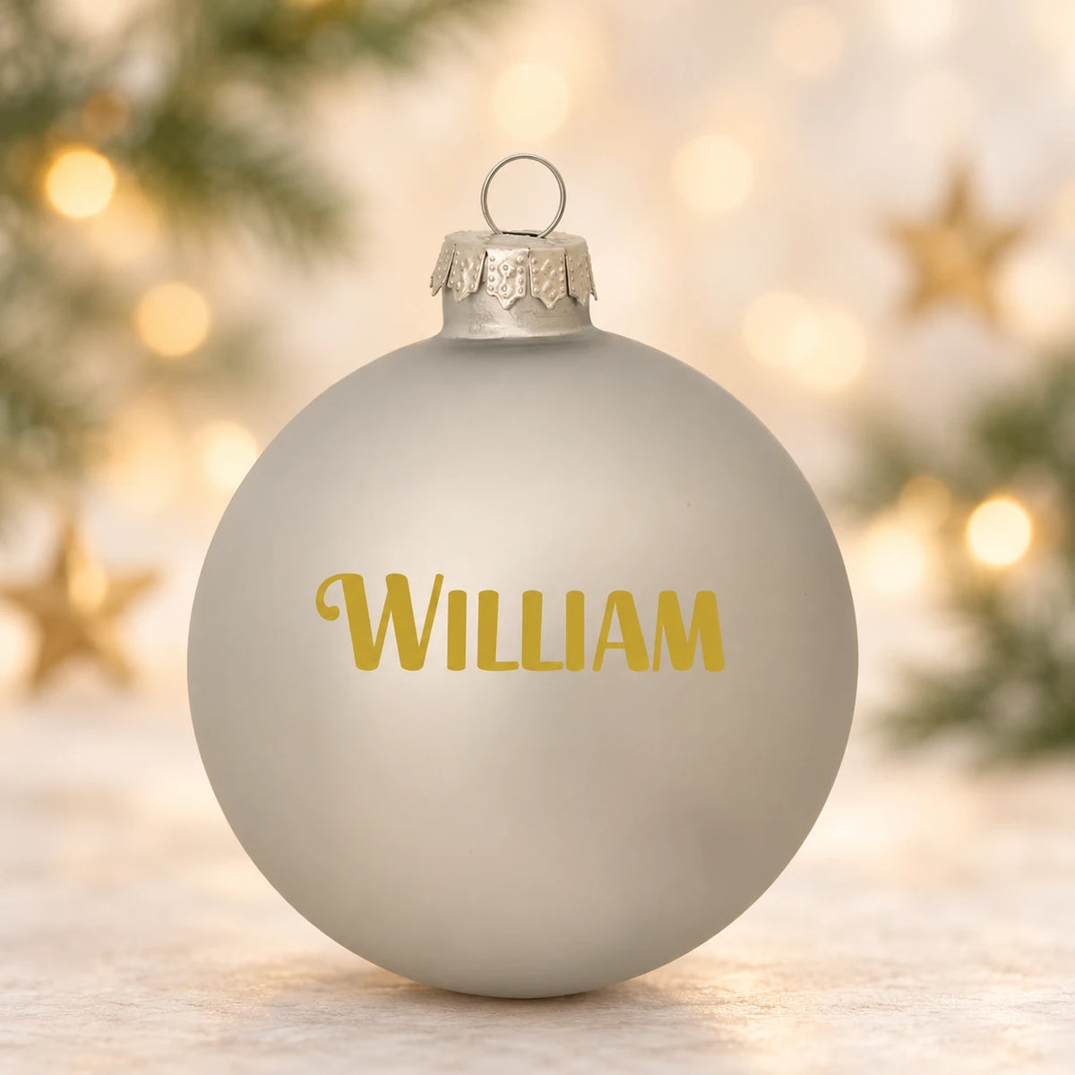 Mat sølv julekugle med navnet William på diffus julebaggrund med gran og stjerner
