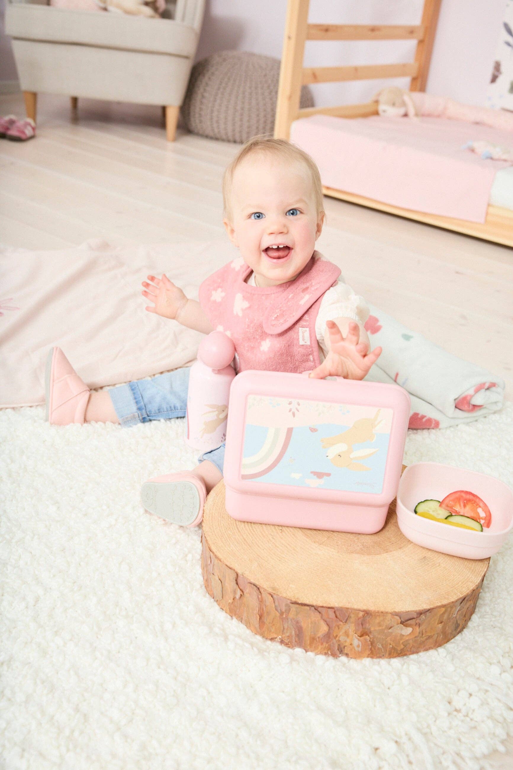 Lyserødt Sterntaler Hase Hanni madkassesæt og drikkedunk i brug af glad baby på gulvtæppe.
