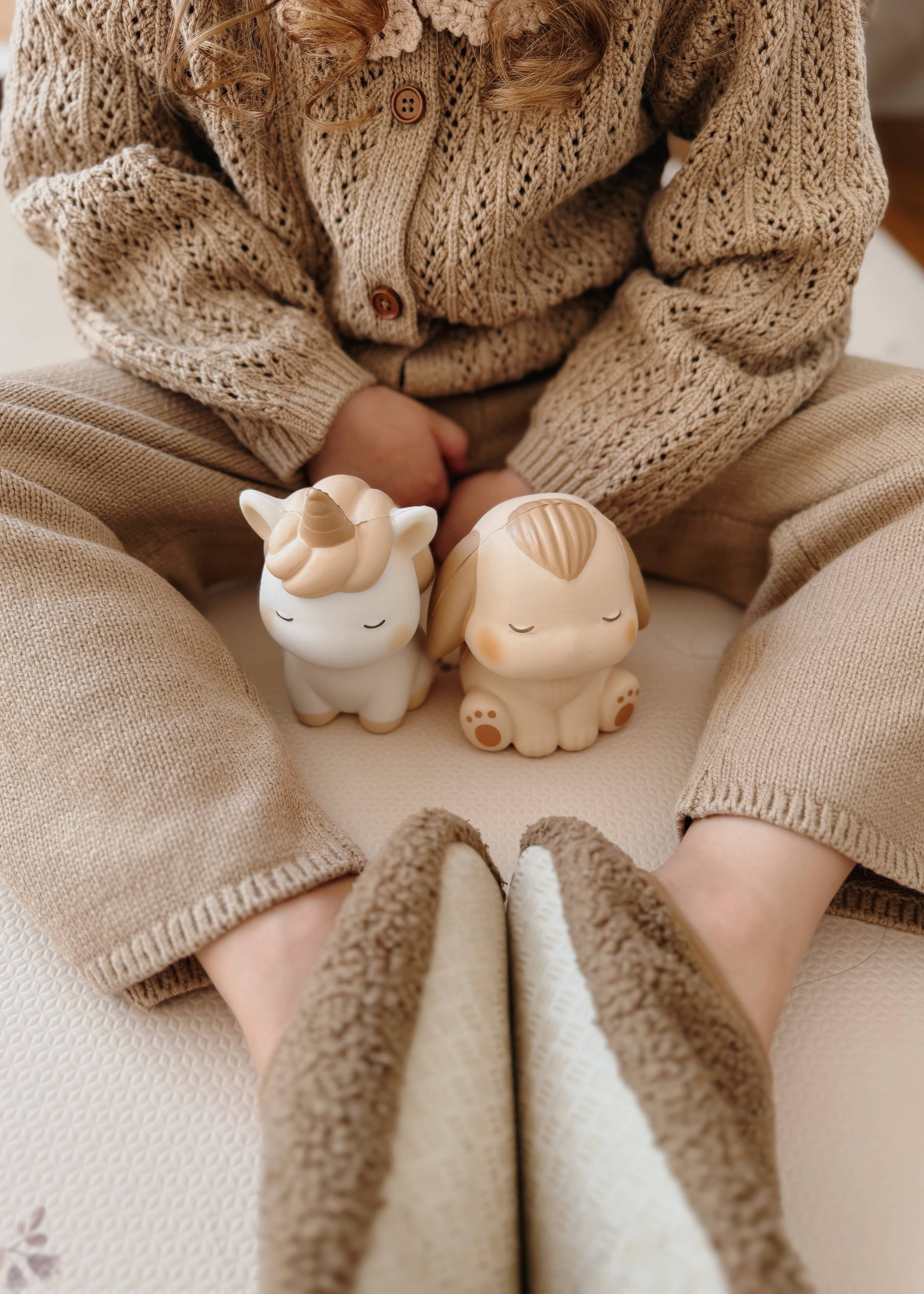 Et barn sidder med Squichymals Uniboo enhjørning og en sød kanin squishy i beige farver.