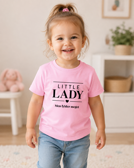 Smilende lille pige i lyserød t-shirt med teksten Little Lady og eget navn.