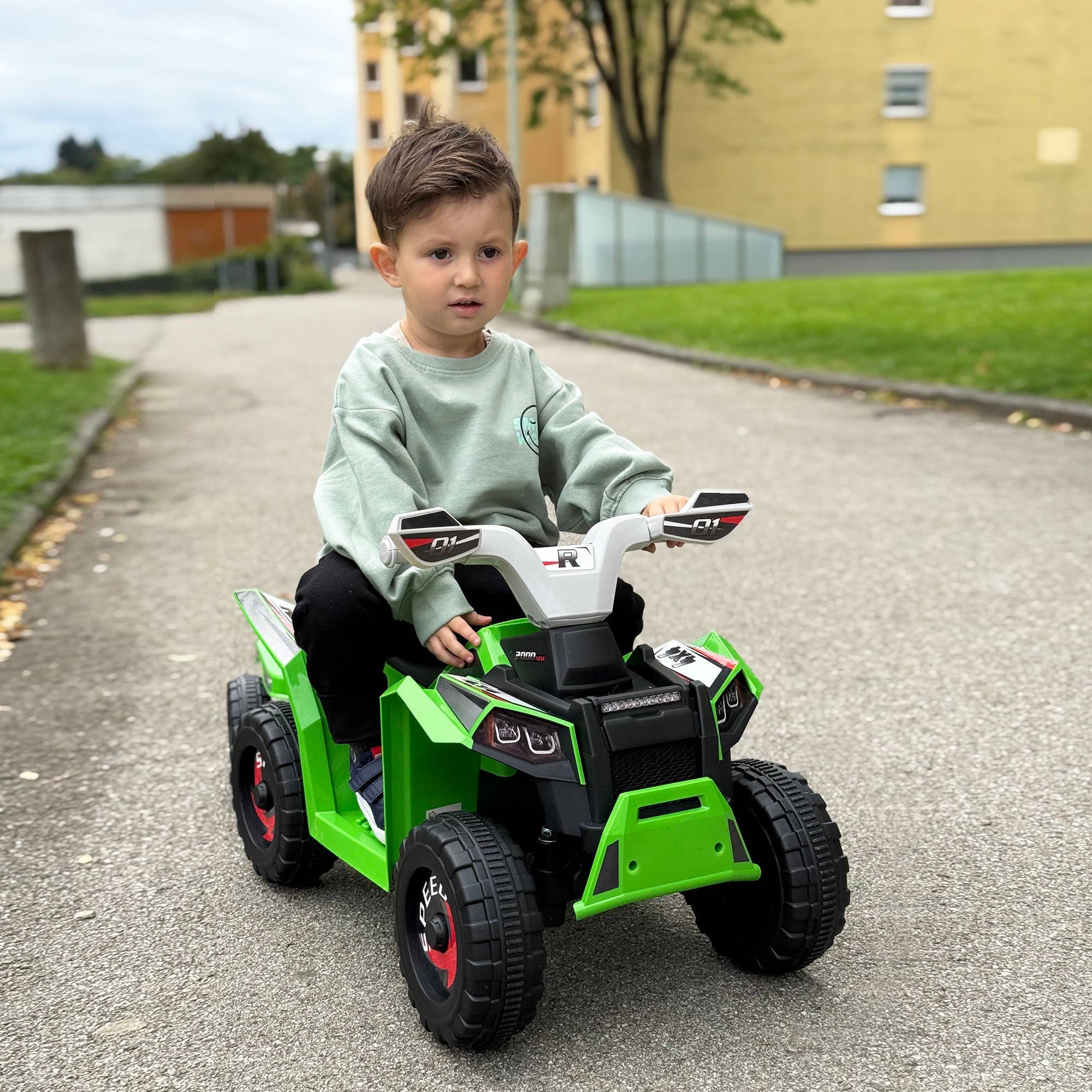 Lille dreng der kører på en grøn elektrisk børnequad udenfor på en sti.