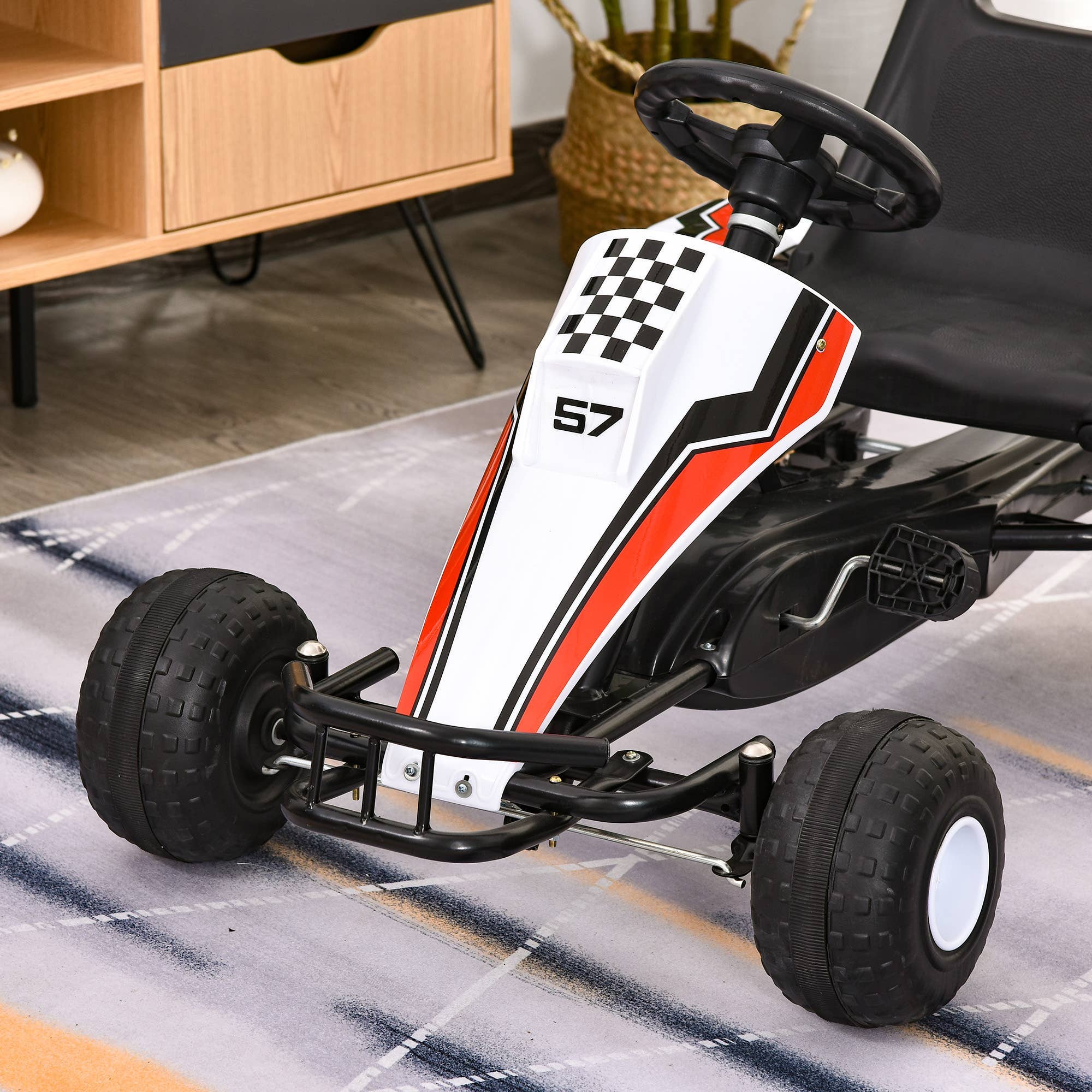 Hvid gokart pedalbil til børn med nummer 57 og racergrafik på et tæppe indendørs.