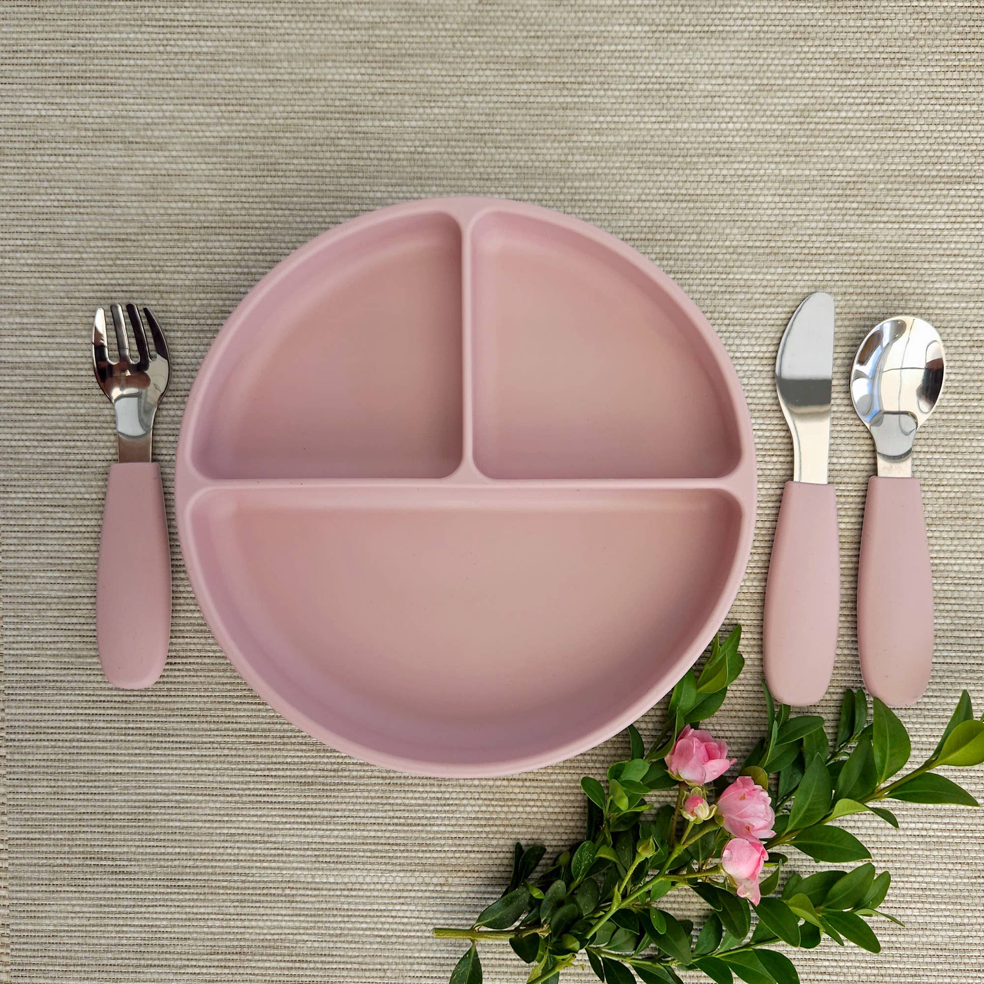 Lys mauve opdelt silikonetallerken til børn vist med matchende bestik og lyserøde blomster.