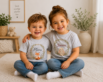 To smilende børn i grå t-shirts med navne og skovdyr motiver fra Skovens blomsterdrøm kollektionen.