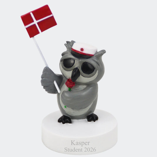 Grå uglefigur med rød studenterhue, rød rose og Dannebrog på hvid sokkel