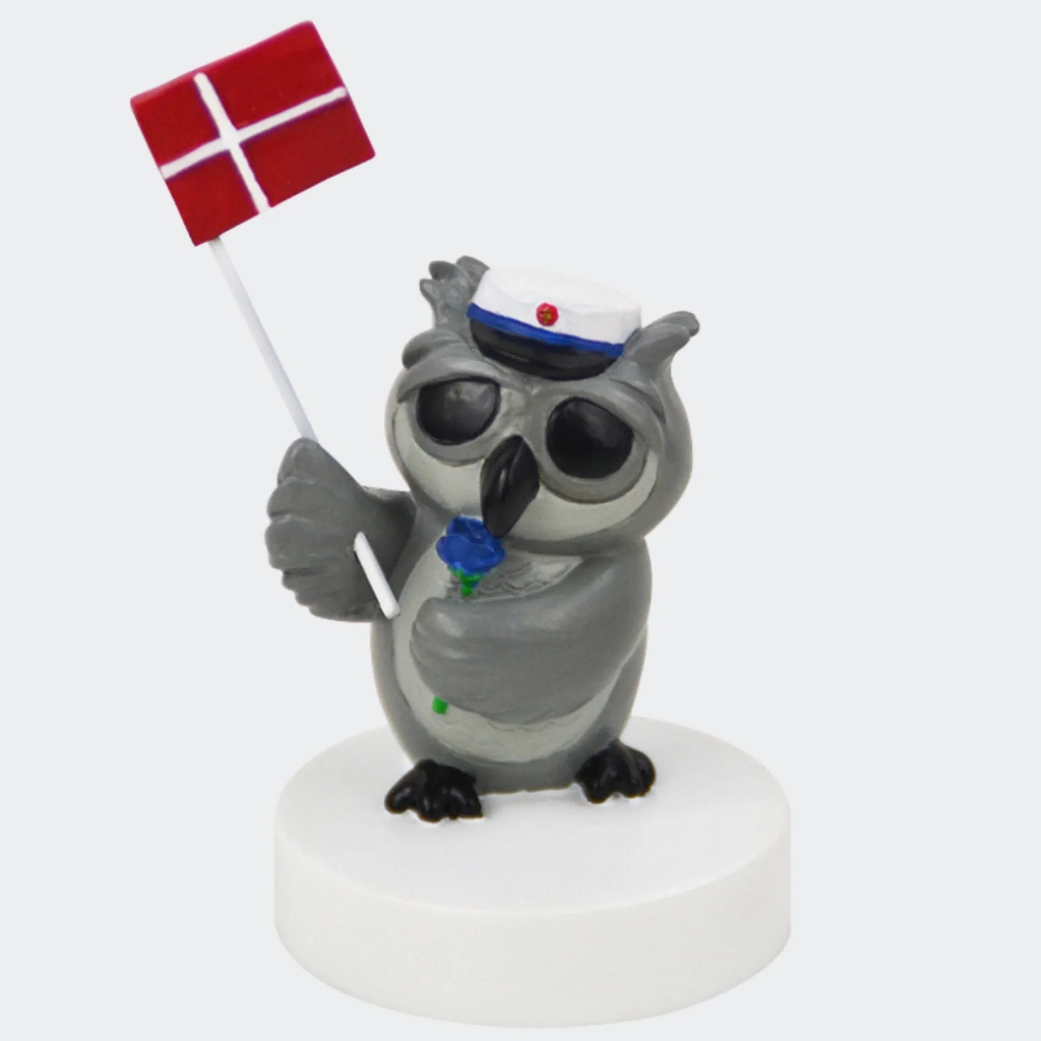 Grå uglefigur med blå studenterhue, blå rose og Dannebrog på hvid sokkel