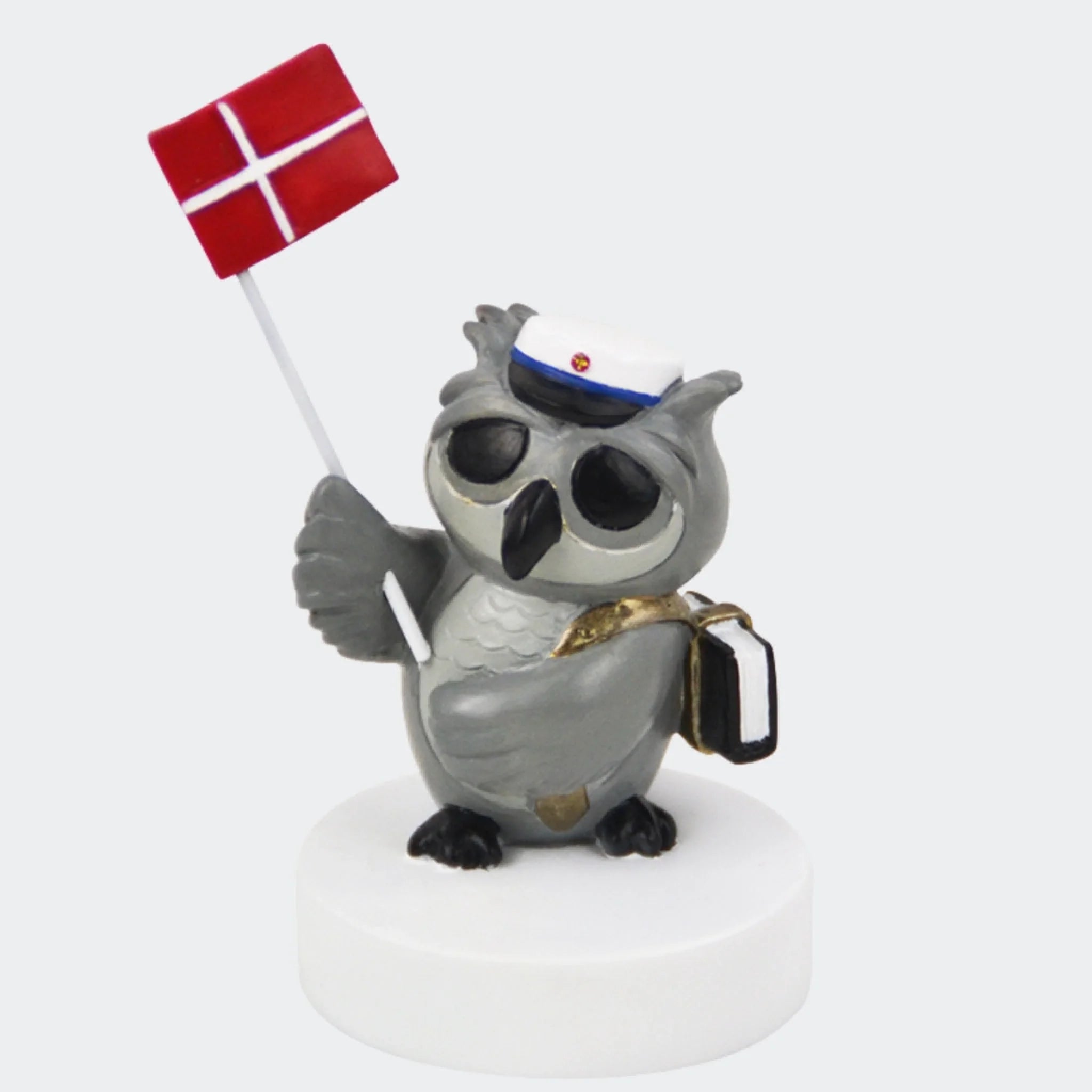 Grå uglefigur med blå studenterhue og Dannebrog på hvid sokkel