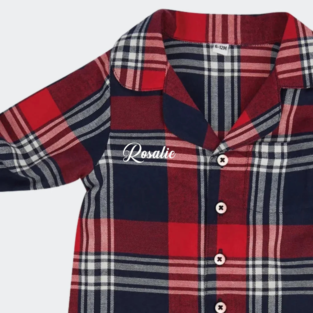 Smilende baby i rød og blå ternet jumpsuit pyjamas med navnet Tristan broderet.