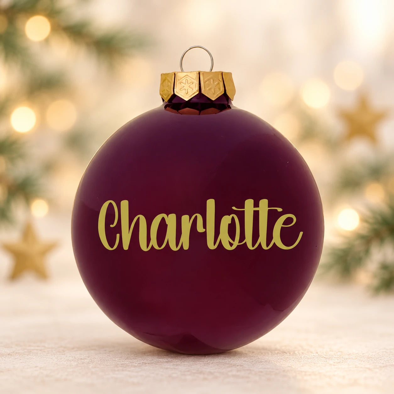Blank bordeaux julekugle med navnet Charlotte på diffus julebaggrund med gran og stjerner