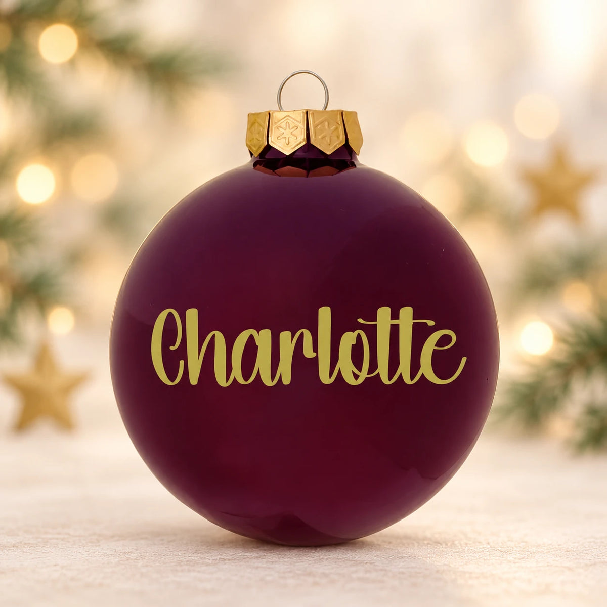 Blank bordeaux julekugle med navnet Charlotte på diffus julebaggrund med gran og stjerner