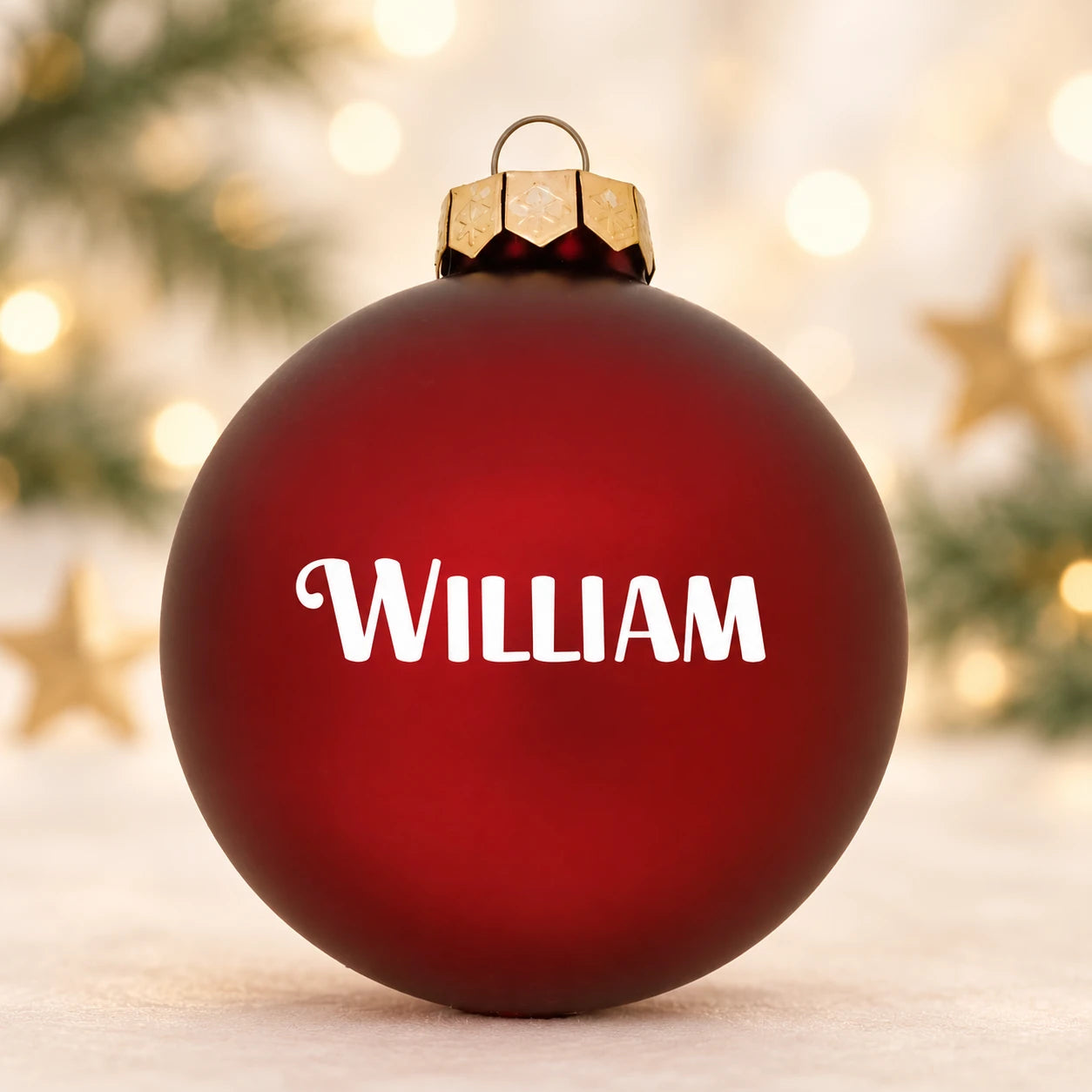 Mat rød julekugle med navnet William på diffus julebaggrund med gran og stjerner