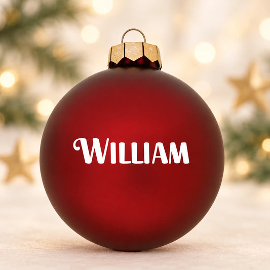 Mat rød julekugle med navnet William på diffus julebaggrund med gran og stjerner