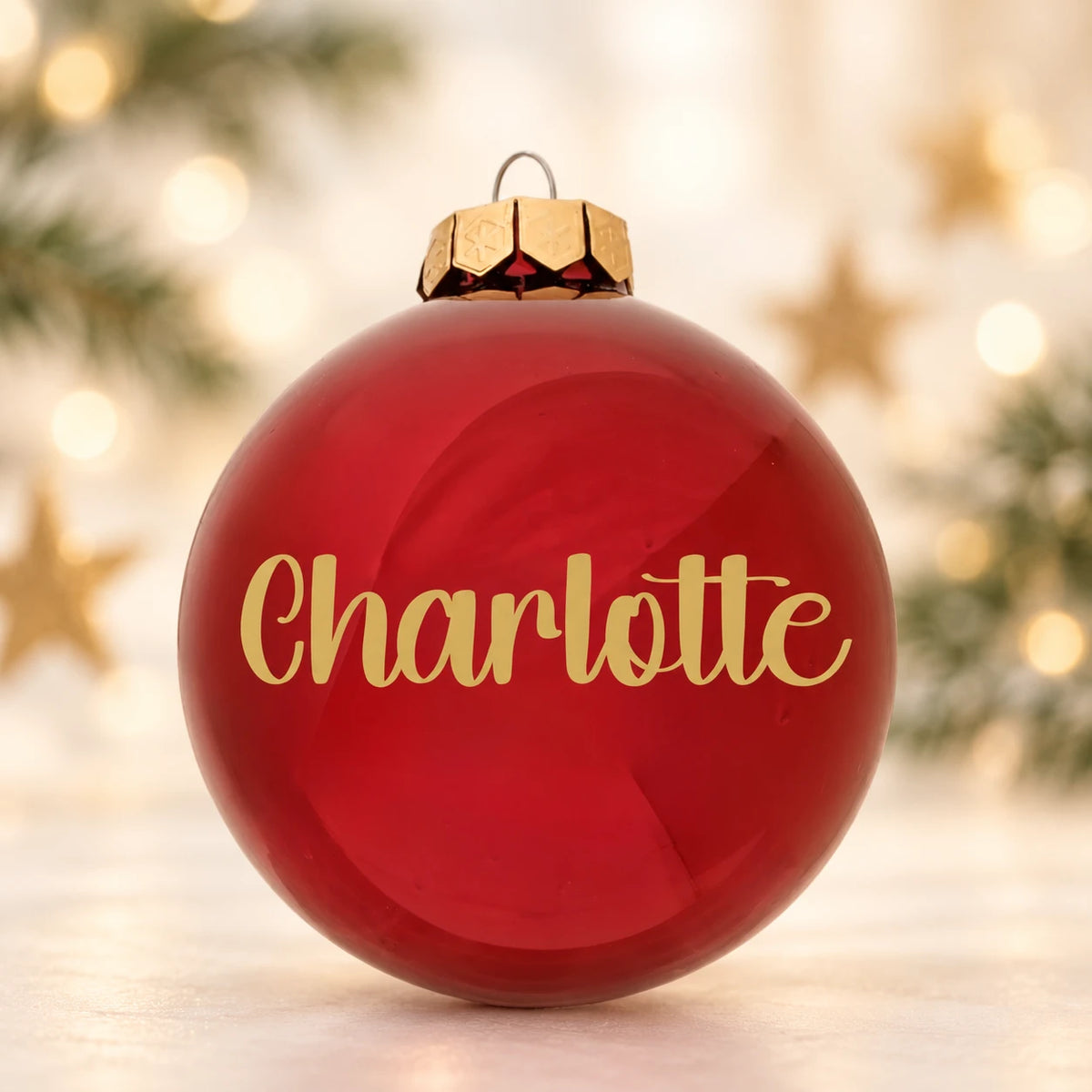 Blank rød julekugle med navnet Charlotte på diffus julebaggrund med gran og stjerner