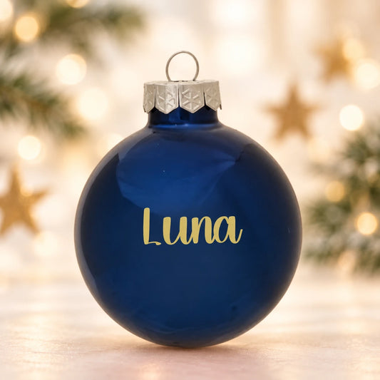 Blank kongeblå julekugle 57 mm med navnet Luna på diffus julebaggrund med gran og stjerner