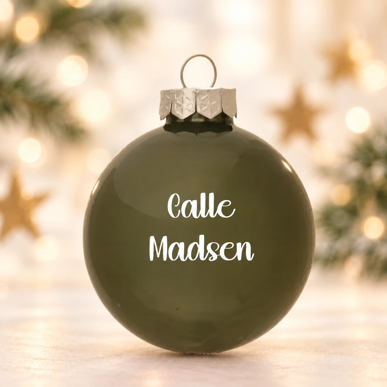 Mat olivengrøn julekugle 57 mm med navnet Calle Madsen på diffus julebaggrund med gran og stjerner