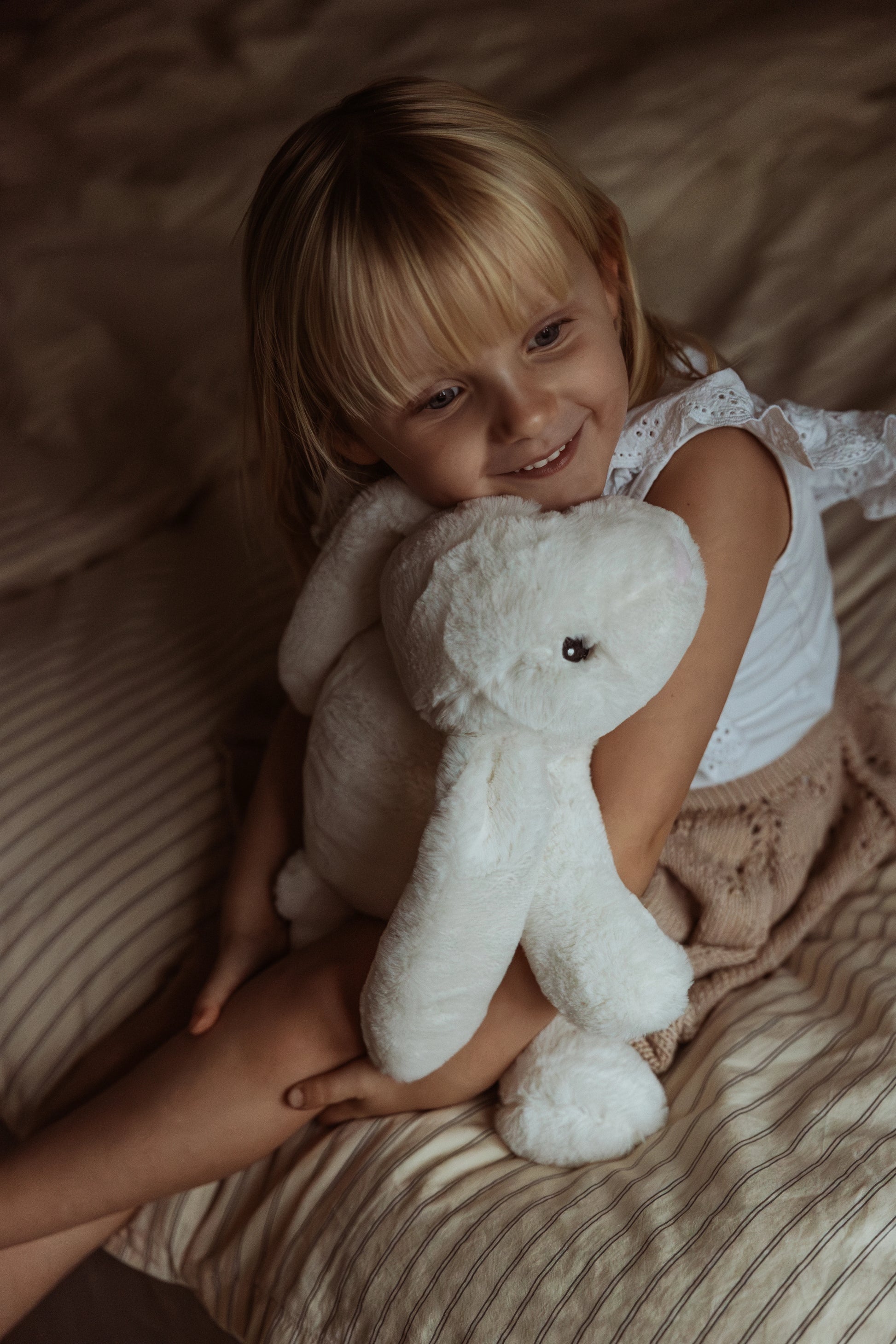 Sød pige krammer en hvid tyngdekanin på en seng