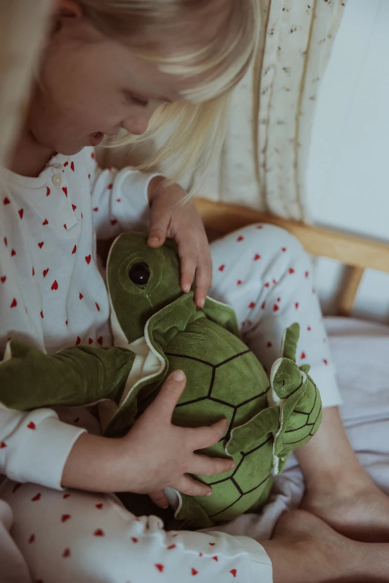 Barn holder en grøn tyngdeskildpadde i seng iført hvid pyjamas