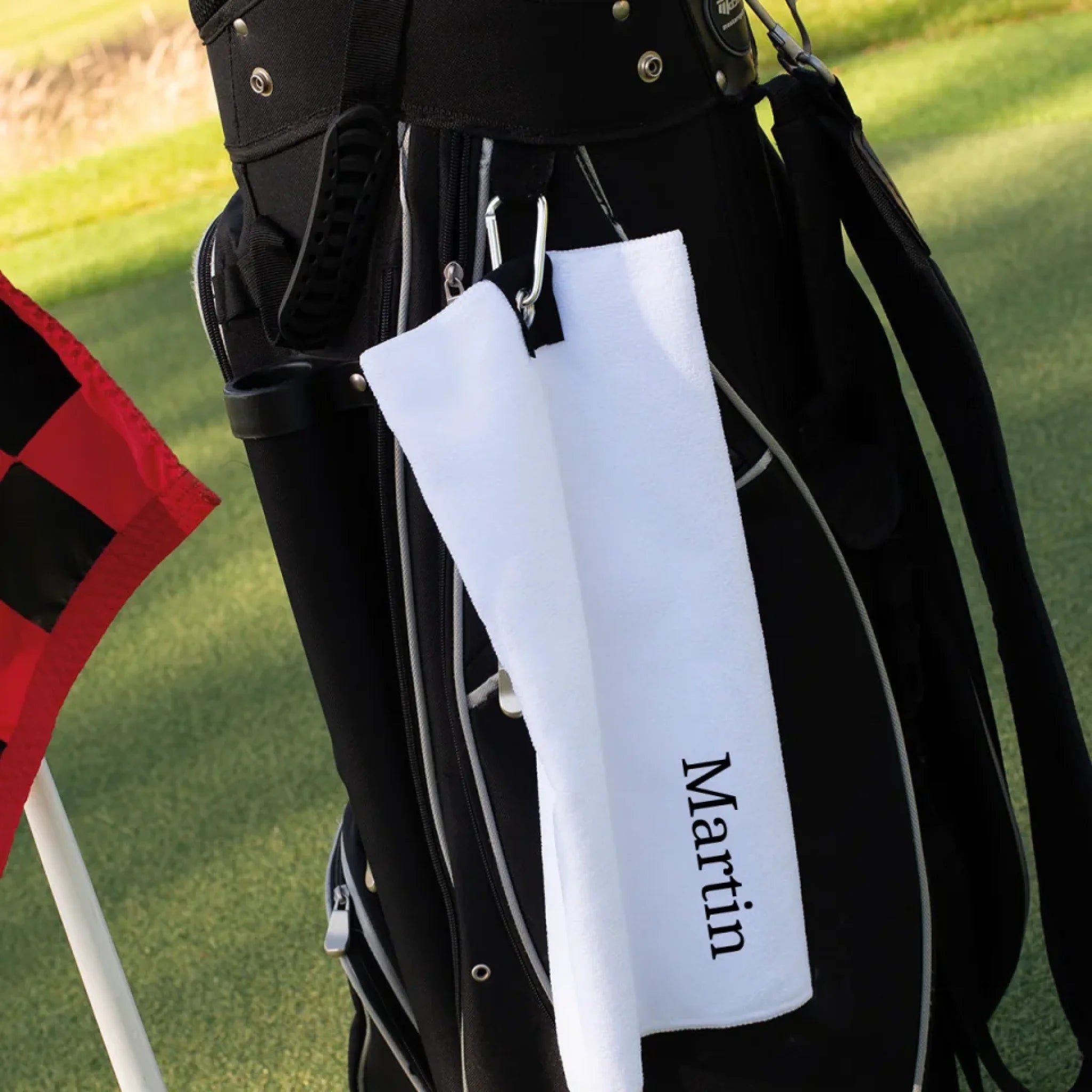 Hvidt golfhåndklæde med navn hængende på en golfbag
