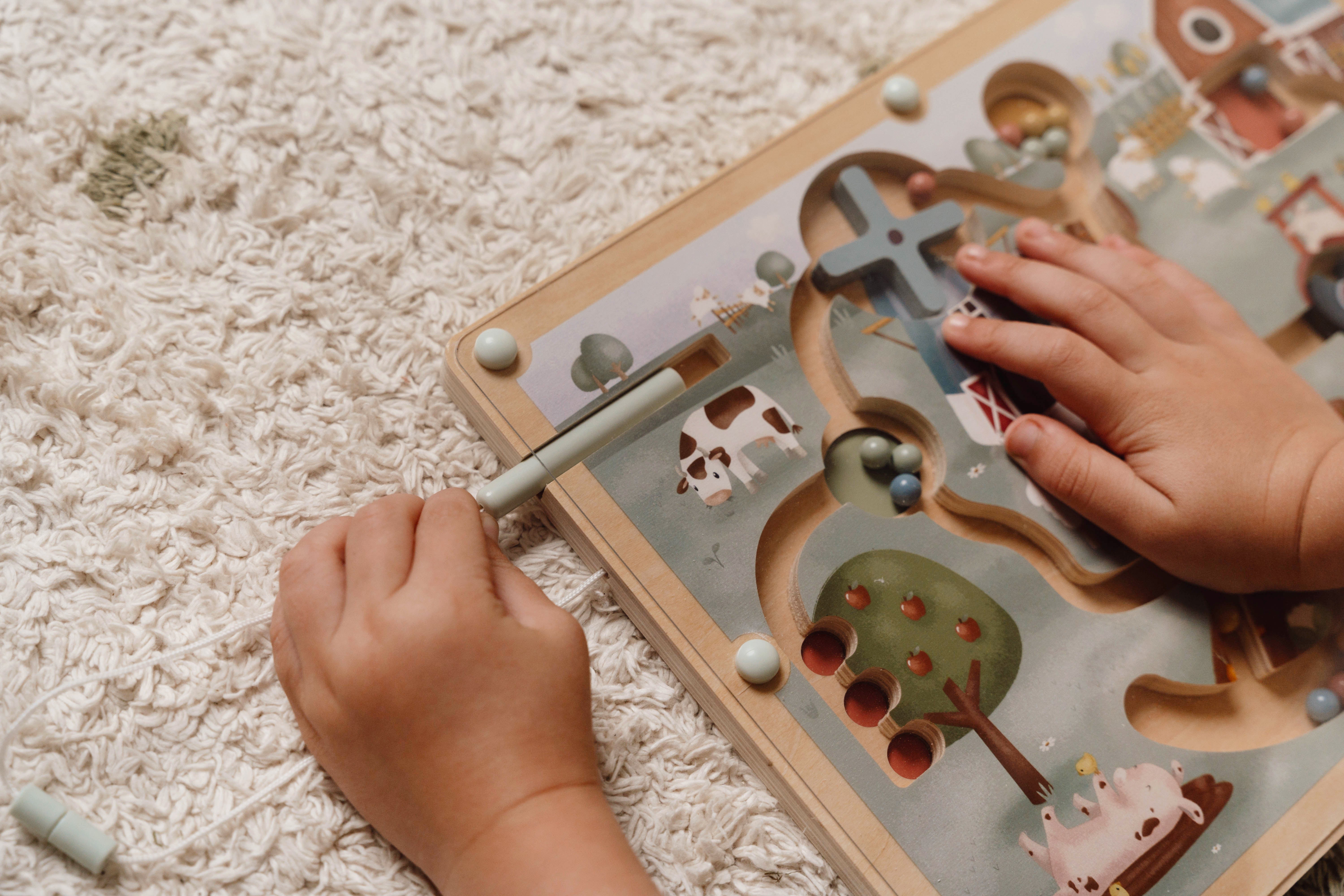 Barns hænder leger med Little Farm magnet labyrint på tæppet.