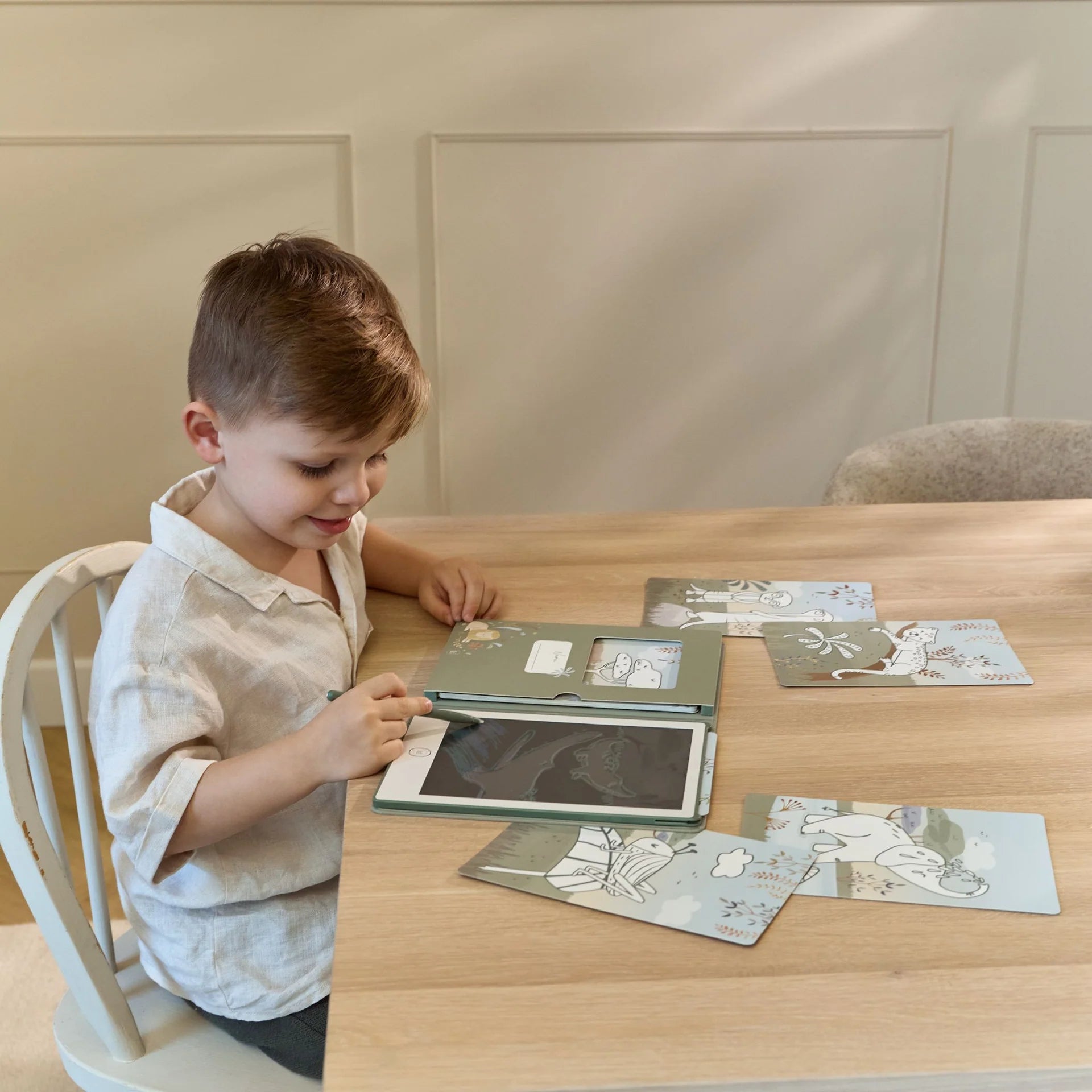 Et lille barn sidder ved et træbord og tegner på en grøn Little Dutch tegnetablet.