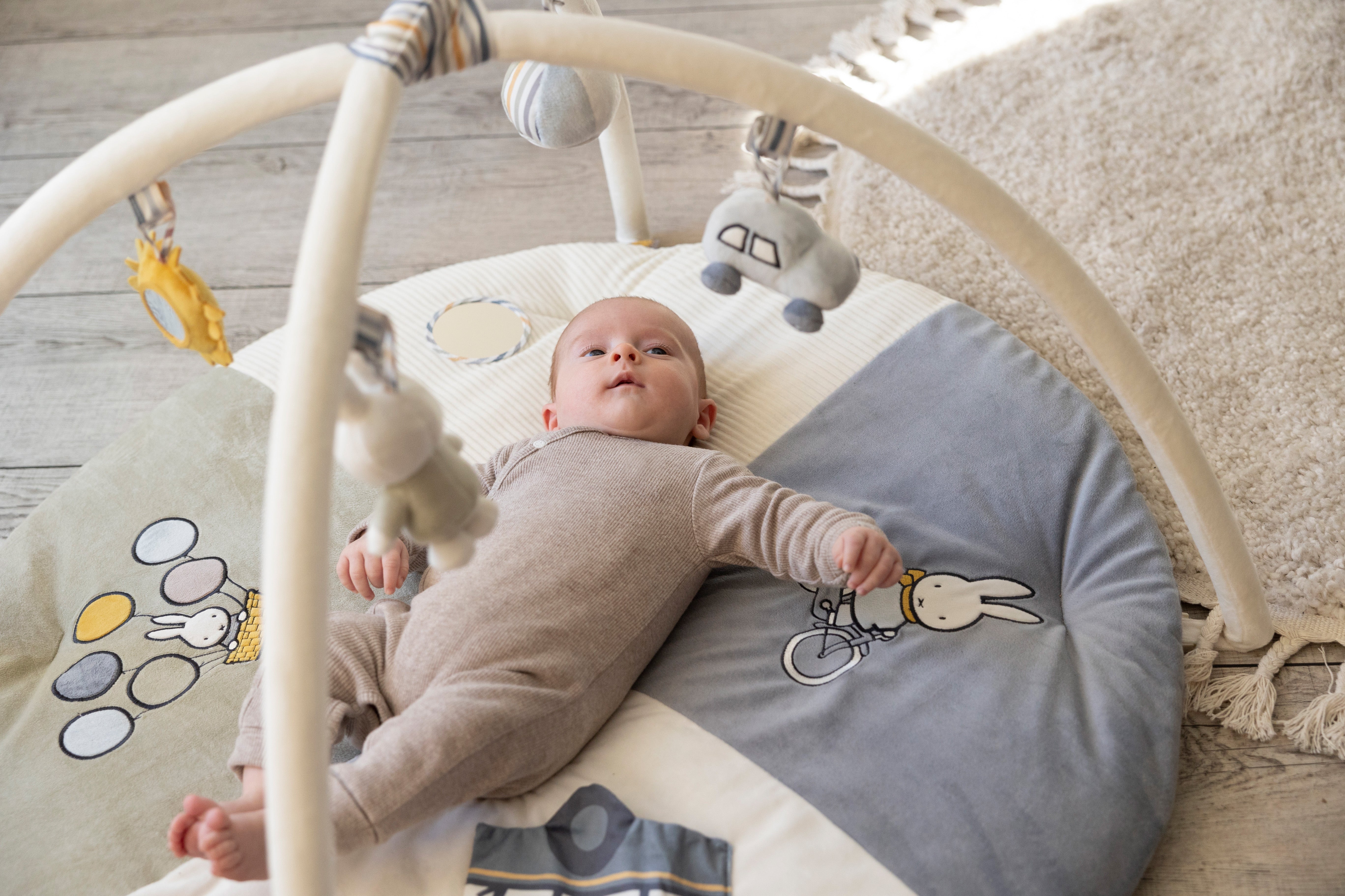 Baby på Miffy aktivitetstæppe med legetøj, blåt tema til stimulering