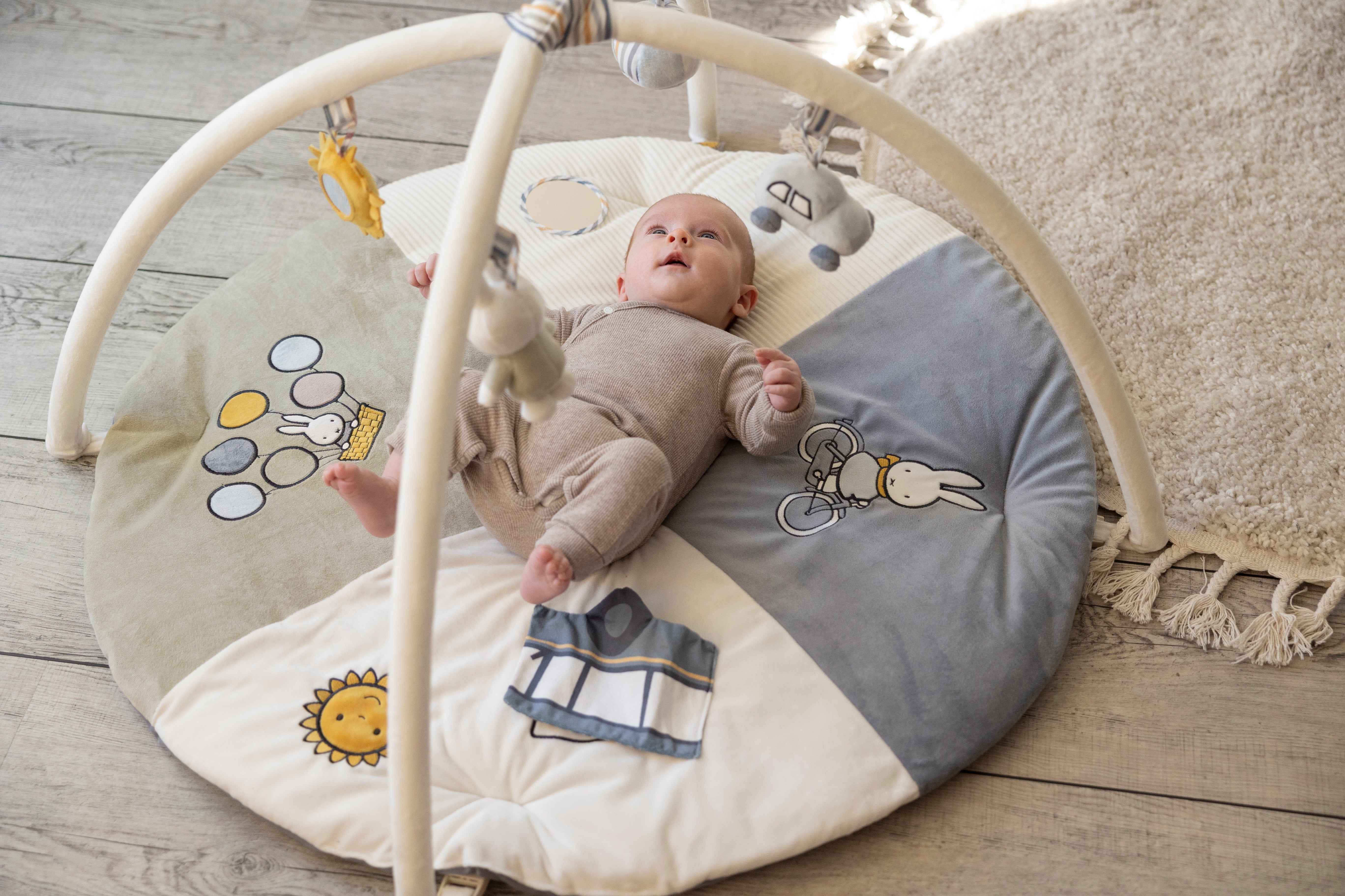 Baby ligger på et Miffy aktivitetstæppe med kanindesign og legetøj