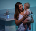 Mor holder baby ved puslebordet med vågelampe i mørkt rum