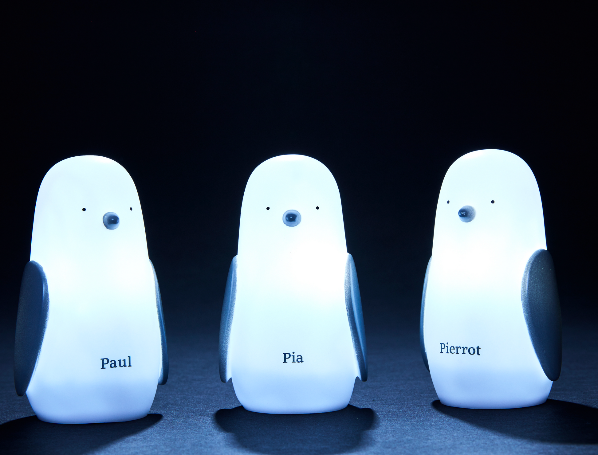 Tre lysende pingvinlamper på sort baggrund med navnene Paul, Pia, Pierrot