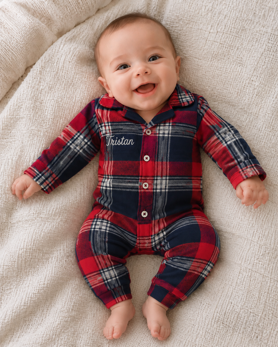 Smilende baby i rød og blå ternet jumpsuit pyjamas med navnet Tristan broderet.