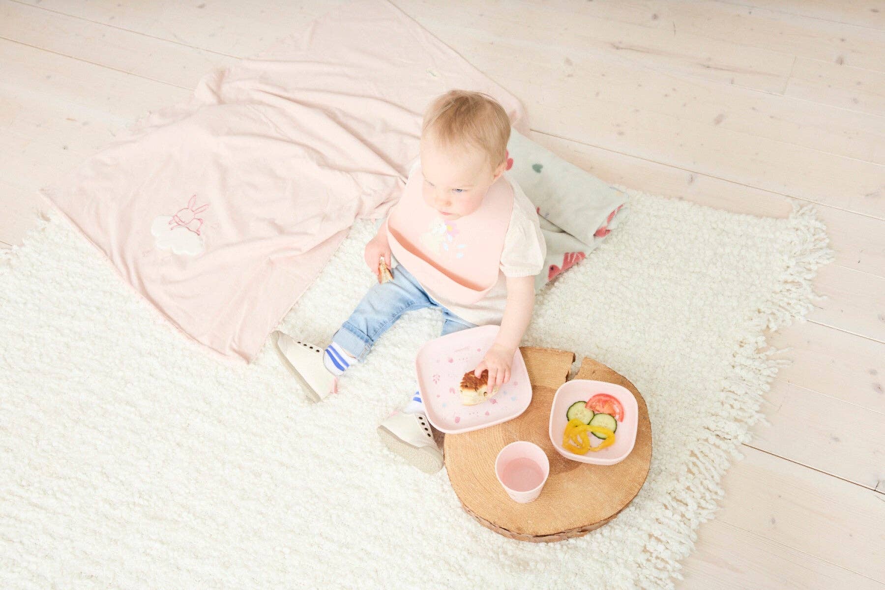Baby der sidder på et tæppe og spiser med lyserødt Sterntaler Hase Hanni servicesæt.