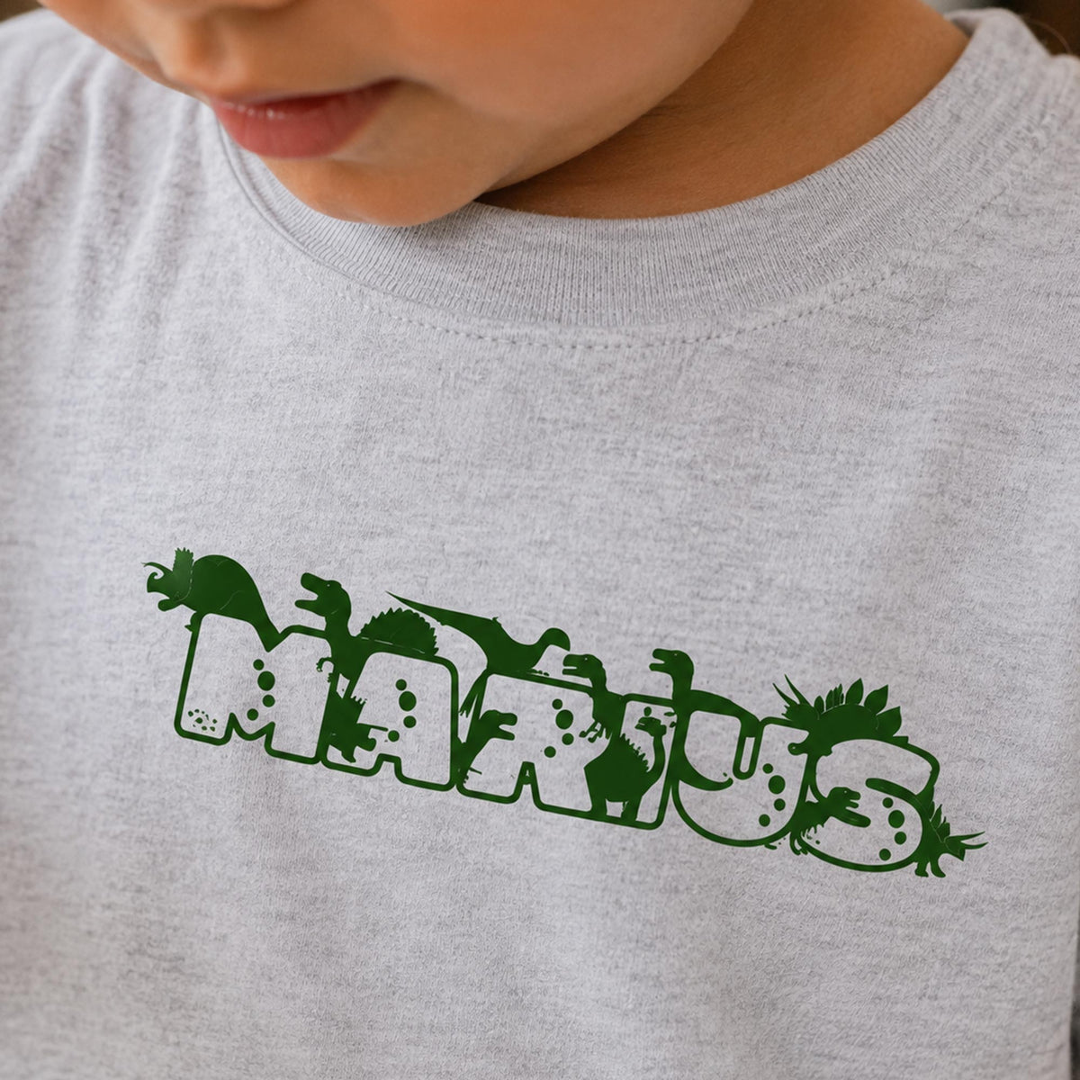 Lysegrå t-shirt til børn med navnet Marius i grøn dino skrift.