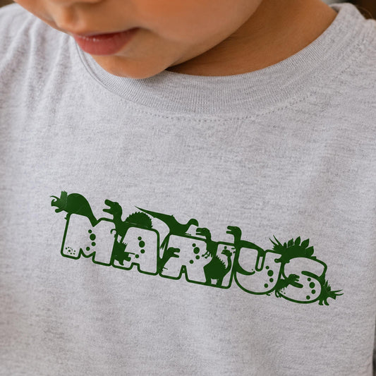 Lysegrå t-shirt til børn med navnet Marius i grøn dino skrift.