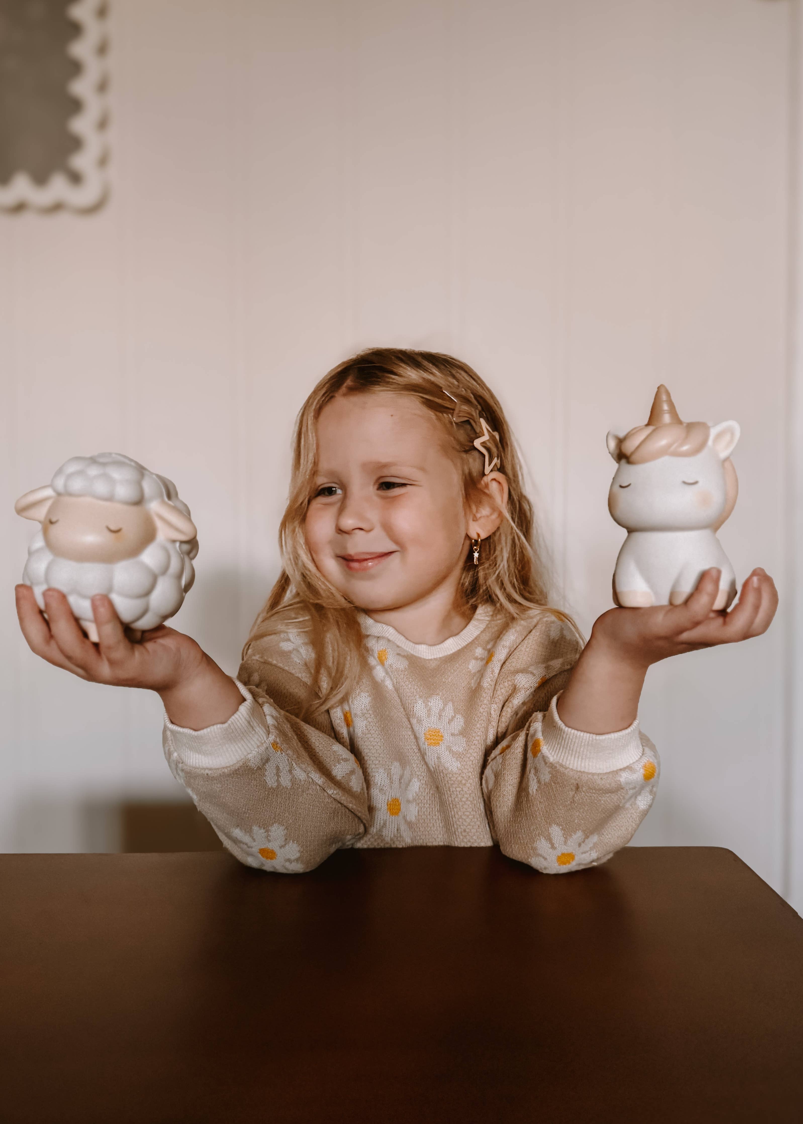 En lille pige der sidder ved et bord og holder Squichymals fåret og enhjørningen.