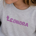 Lysegrå t-shirt til børn med personligt navn Leonora i lilla unicorn skrift.