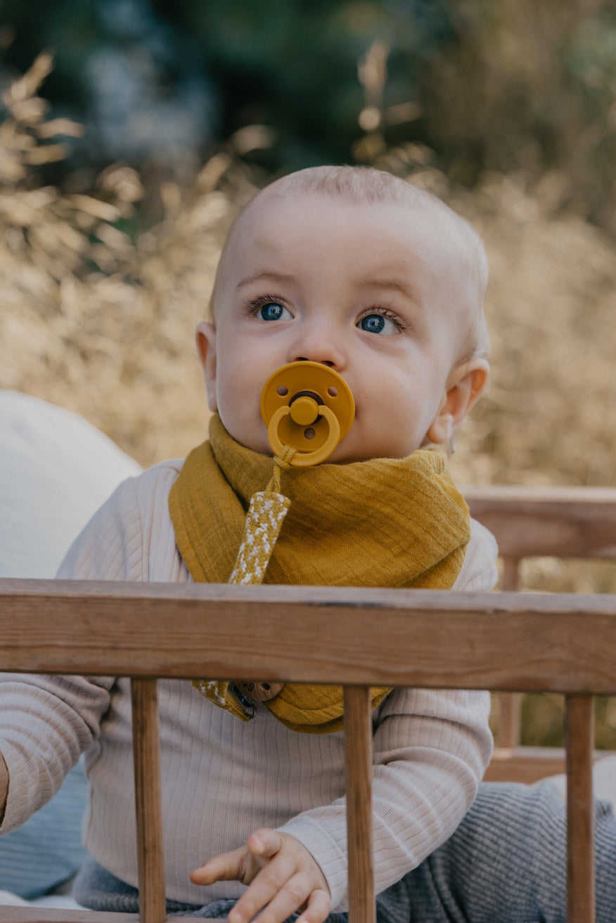 Baby i seng med gul BIBS sut og suttesnor i matchende farver