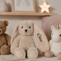Blød beige kaninbamse med navnet Elina broderet på øret i et hyggeligt børneværelse.