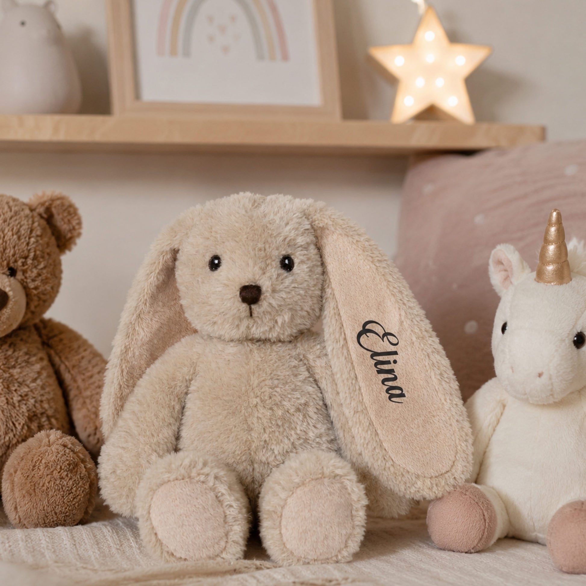 Blød beige kaninbamse med navnet Elina broderet på øret i et hyggeligt børneværelse.