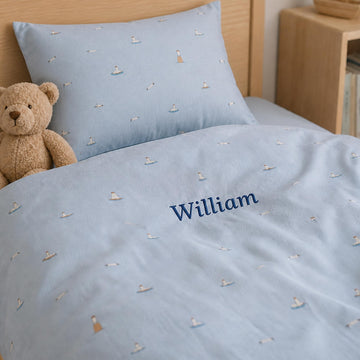 Lyseblåt sengetøj til børn med broderet navn William og lille bamse i sengen.