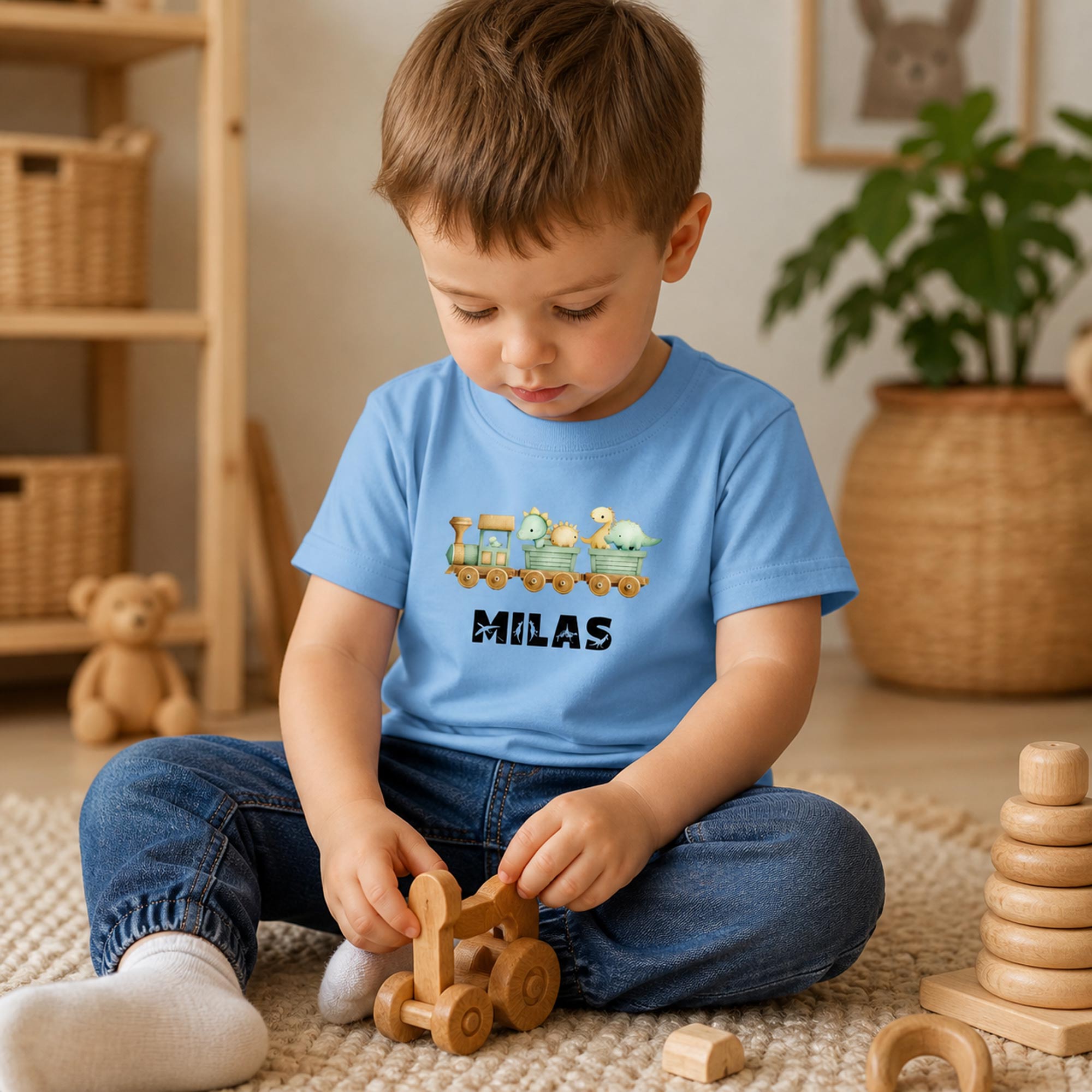 Lille dreng i lyseblå t-shirt med dino tog og navnet Milas leger på gulvet.