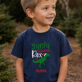 Dreng i en navy blå Santa Saurus Rex t-shirt med juledinosaur og personligt navn.