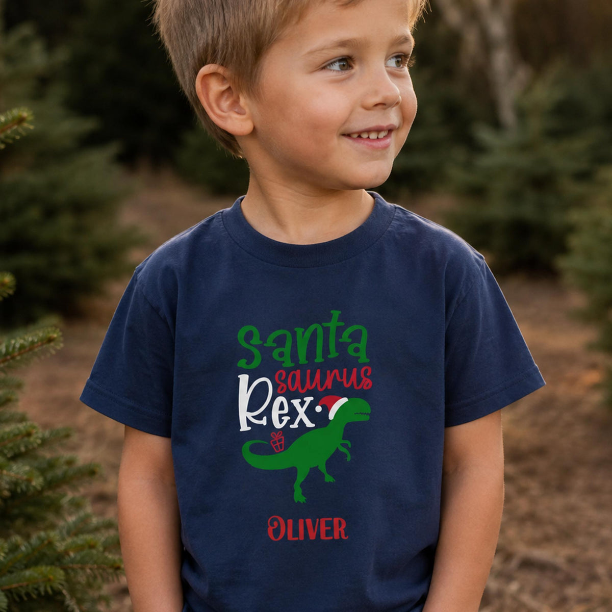 Dreng i en navy blå Santa Saurus Rex t-shirt med juledinosaur og personligt navn.